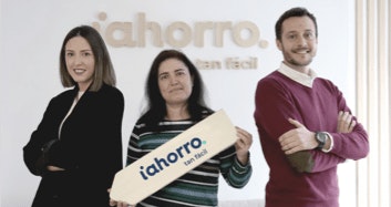 Tres empleados de iAhorro posan en nuestras oficinas. La persona del centro sostiene un cartel con el logo de la empresa.